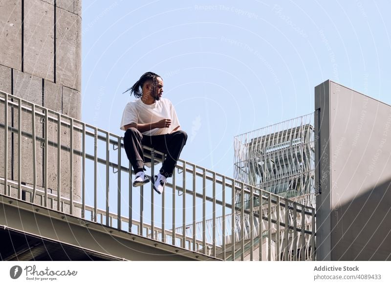 Black male sitting on bridge man city street railing african american urban sunny daytime young casual lifestyle leisure rest relax modern structure