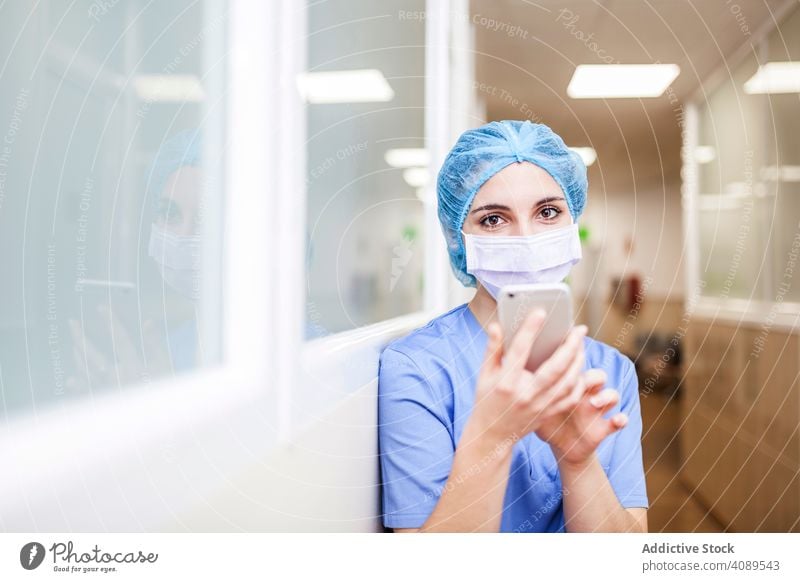 Female Surgery using her smartphone in a hospital job posture weary indoors hat wall operating room professional nurse female hallway white copy space doctor