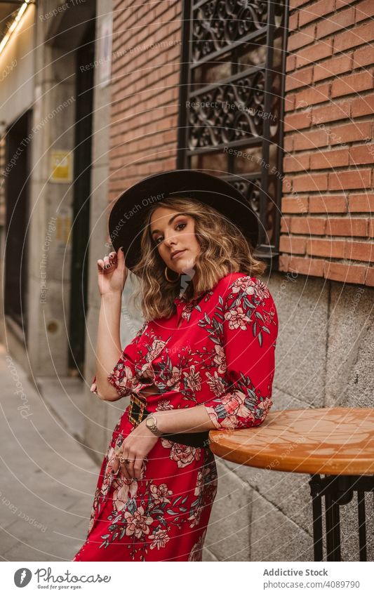 Stylish lady leaning on table on street woman stylish old building elegant young city female confident positive hat dress fashion voguish glamour exterior aged
