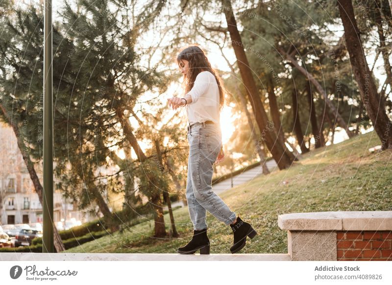 Young woman walking on border in park balance outstretched arms sunny daytime young casual female focused concentrated lifestyle leisure rest relax harmony