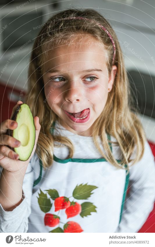 Girl with avocado licking lips girl kitchen tasty fresh vitamin kid home looking away child apron food cooking delicious yummy face expression green lifestyle