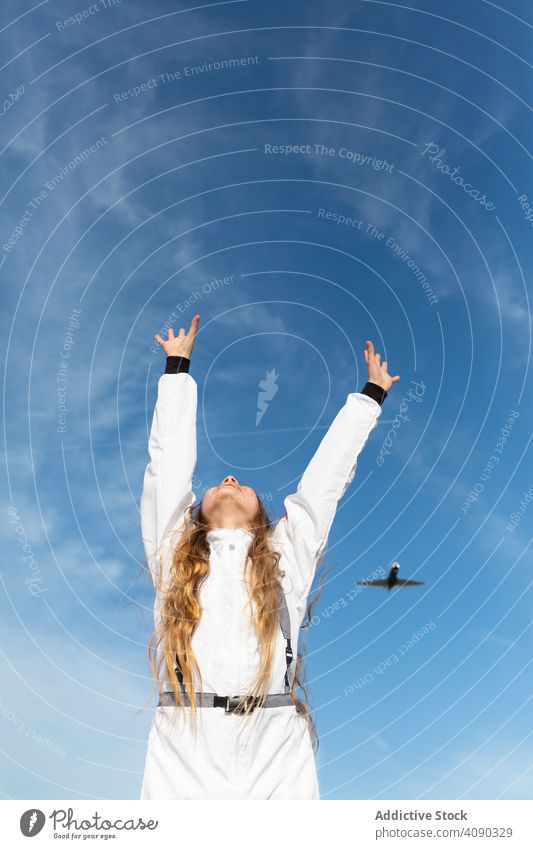 Cheerful teenager trying to reach flying plane girl reaching hands up smiling sky clouds sunny daytime happy excited cheerful joy aircraft flight lifestyle