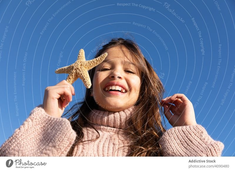Smiling girl showing starfish near sea beach smiling touching hair sunny daytime tourism holiday kid child teen nature water vacation ocean little cheerful cute