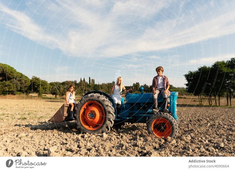 group of young friends siting and looking at camera on a blue tractor in a rural terrain farm grandchildren field riding together sunny daytime rustic