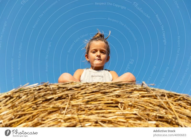 Girl sitting on hay roll girl farm sky cloudless blue sunny daytime kid child field dried grass straw summer countryside rural rustic harmony idyllic freedom