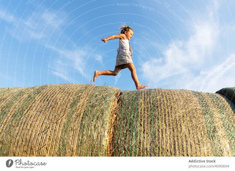 Barefoot girl running on haystacks farm sky clouds sunny daytime nature lifestyle leisure teen kid child barefoot dried grass straw rolls countryside rustic