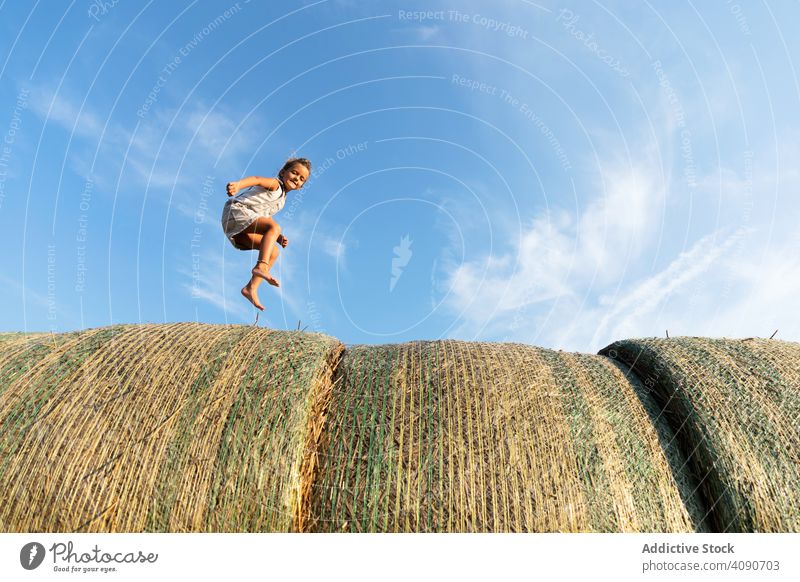 Barefoot girl running on haystacks farm sky clouds sunny daytime nature lifestyle leisure teen kid child barefoot dried grass straw rolls countryside rustic