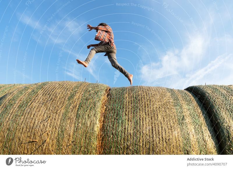 Barefoot boy running on haystacks farm sky clouds sunny daytime nature lifestyle leisure teen kid child barefoot dried grass straw rolls countryside rustic