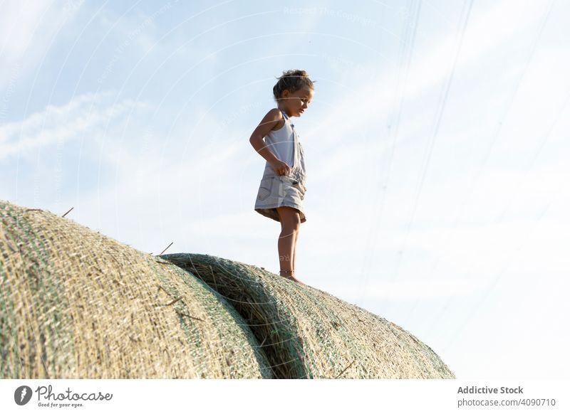 Barefoot girl standing on haystacks farm sky clouds sunny daytime nature lifestyle leisure teen kid child barefoot dried grass straw rolls countryside rustic