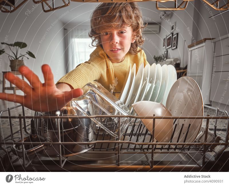 Boy near open dishwasher boy kitchen routine housework dishware home closed eyes kid child wavy hair pajamas kitchenware technology equipment cozy modern tired
