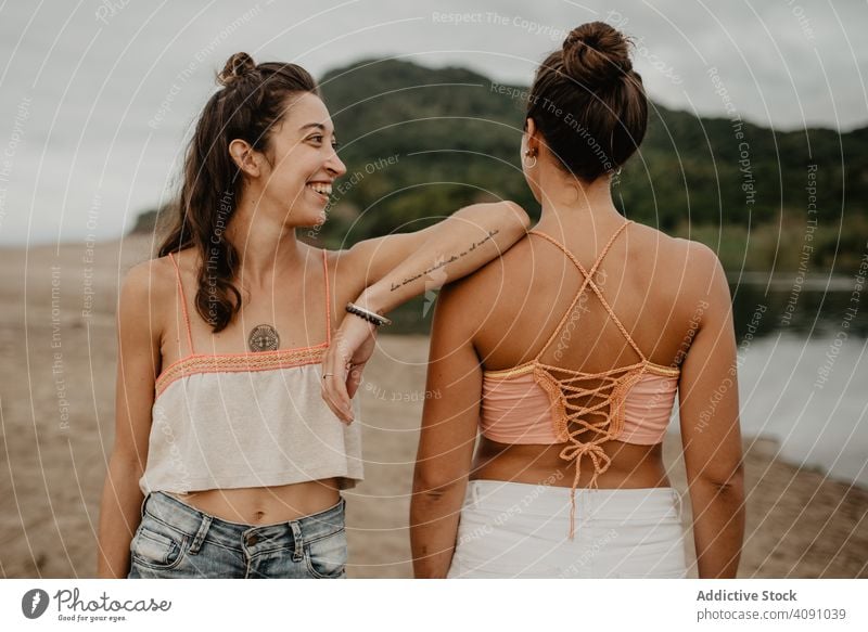 Anonymous tattooed woman leaning on friend on beach friends together shoulder arm women summer young friendship writing inscription shore coast swimwear rest