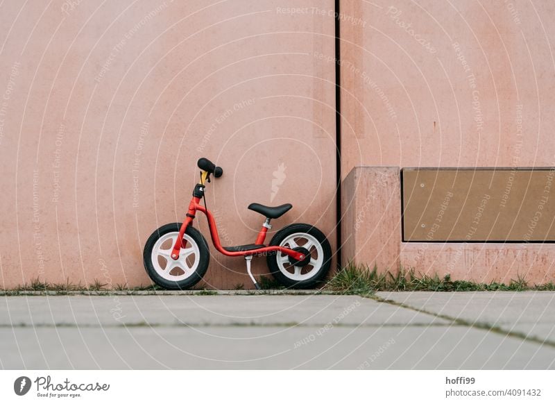 a red wheel, parked in front of a pink wall impeller Children's bike Minimalistic Red Pink child's playbike Bicycle Cycling Infancy Wheel Lifestyle Driving