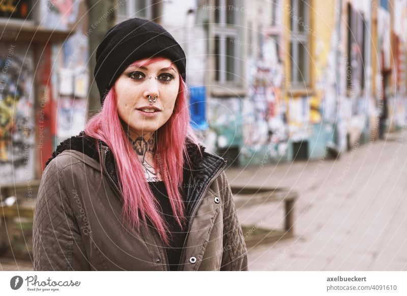 young woman with pink hair, piercings and tattoos in front of graffiti covered houses Young woman Piercing Tattoo real people Subculture Graffiti
