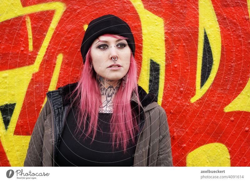 young woman with pink hair, piercings and tattoos in front of graffiti wall Young woman Piercing Tattoo Graffiti E-Girl Hipster real people Graffiti wall