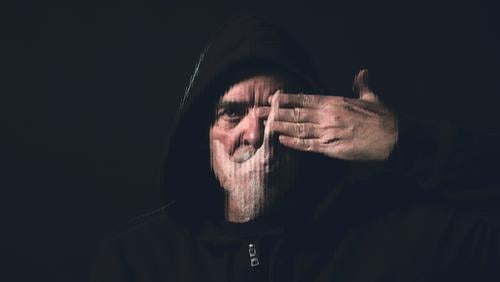 portrait of a man with a hoodie holding a hand in front of his face beard double exposure stripes hands eye mouth silent blind studio black indoor blurred
