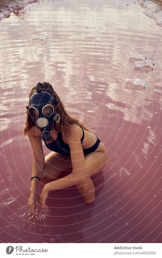 Female in swimwear walking in dirty pool with litter pollution water lake plastic bottle respirator woman swimsuit garbage planet waste save female junk