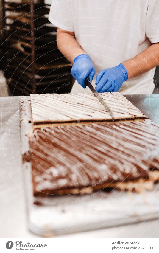 Anonymous cook cutting cake on table confectioner bakery knife pastry sweet fresh kitchen food preparation small business man uniform glove quality dessert