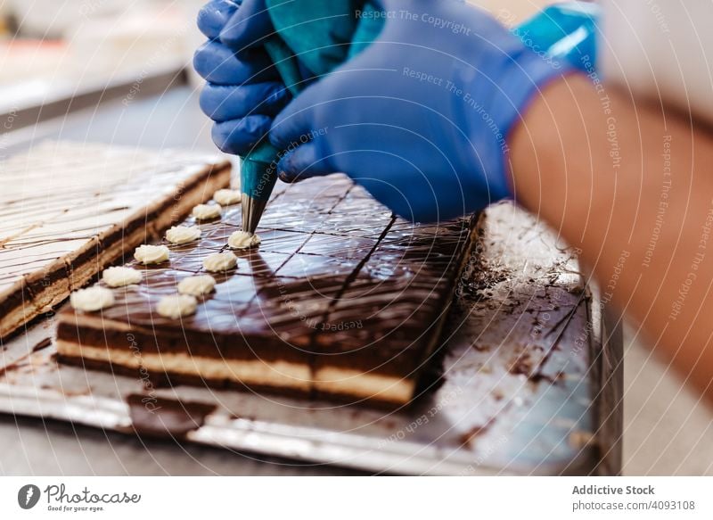 Crop confectioner decorating small cakes bakery cream squeeze chocolate tray cook pastry food fresh quality preparation work commercial traditional occupation
