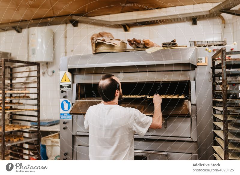 Bald baker checking pastry inside oven man bakery peek work confectioner cook hot process male adult uniform cuisine small business wait heat warm equipment