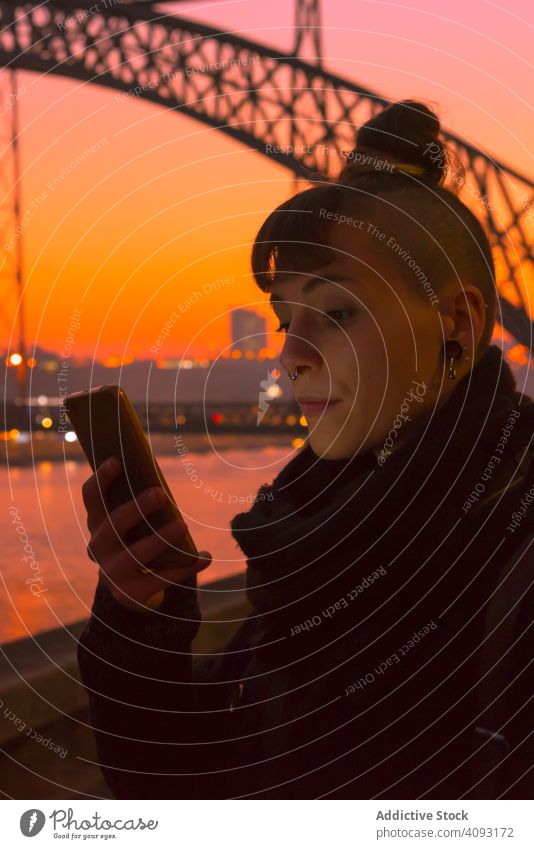 Stylish woman using smartphone on embankment in evening sunset city river stylish young bright female alternative generation subculture trendy device gadget