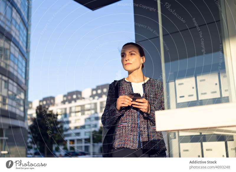 Smiling businesswoman using the cellphone smartphone smile building office entrance street modern city urban female cheerful work wall glass job mobile device