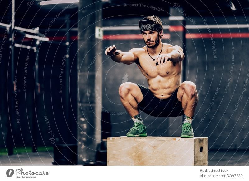 Athletic man jumping on box to improve stamina in gym trainer workout muscular exercise athletic client help fellow squatting sport club bodybuilder athlete