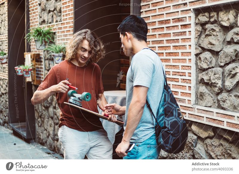 Interested male friend discussing longboard while standing on street discussion share talk attentive casual men urban building pavement conversation bonding