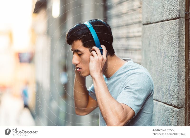Man in headphones listening music on the street man city using streaming content cool joyful modern casual stand sunny town young adult internet online