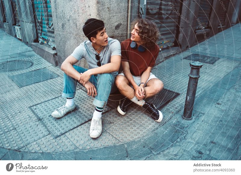Relaxed multiracial male friends talking while resting by corner of building on street positive relaxed millennial discussion pavement cool together