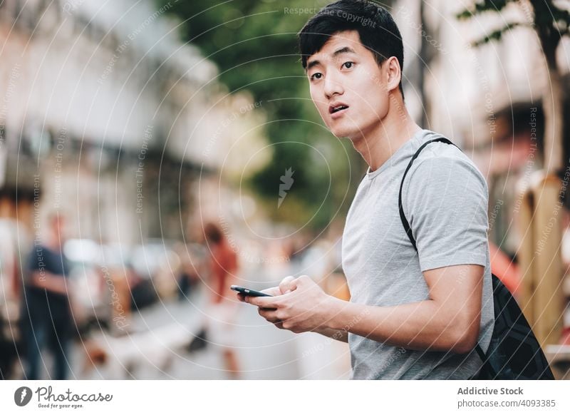 Confused Asian man using smartphone while standing on street confused direction browsing uncertain casual lost amazed search asian ethnic young adult worried