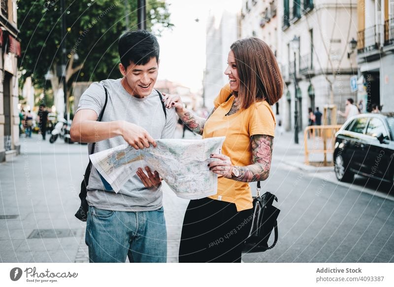 Joyful multiracial tourists checking map and standing on urban street joyful fun lost laugh city direction holding smile search multiethnic asian diverse