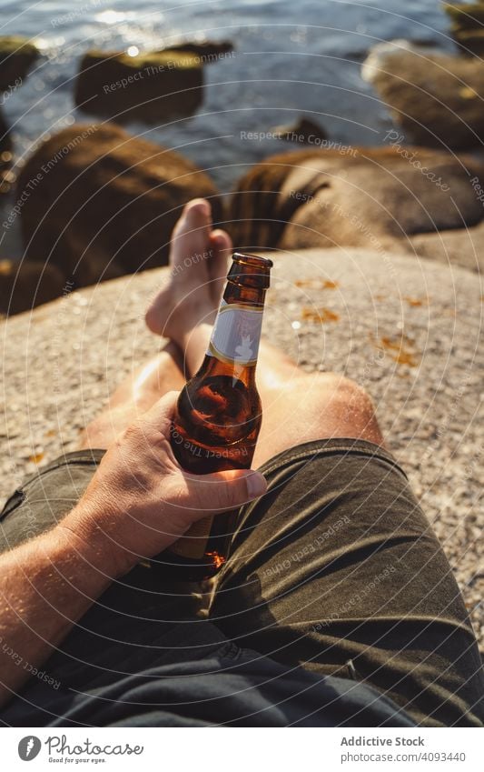 Bottle of beer in hand with seascape on background man barefoot coast sunlight bottle cheers seaside alcohol beach through refreshment party travel outdoors