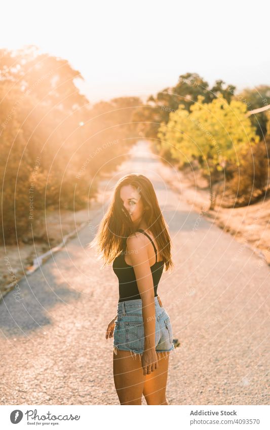 Playful slim woman walking along rural road and looking at camera romantic playful content turn around countryside smile pathway jeans shorts nature happy young