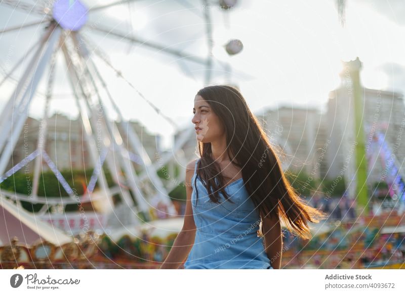 Dreamy woman resting by Ferris wheel in amusement park dreamy summer fairground sundress ferris wheel relaxed calm entertainment wistful long hair attractive