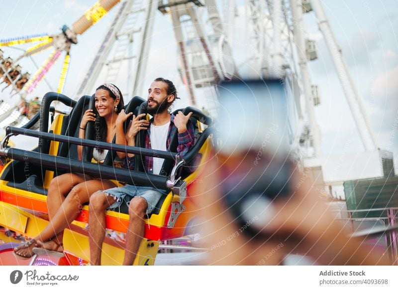 Taking photo of excited couple riding carousel at amusement park ride entertainment taking photo joyful happy casual friend smartphone smile enjoy using