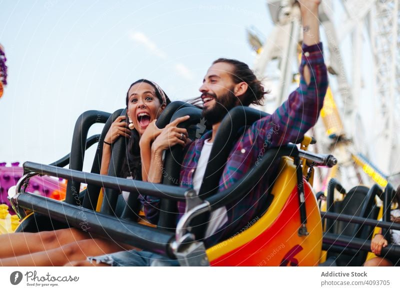 Amused couple riding spinning carousel at fairground amusement park fun ride amazed amused enthusiastic date happy carefree casual smile enjoy attraction