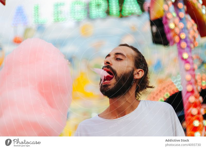 Content man enjoying cotton candy at funfair eat hipster amusement park delighted content happy bearded stand adult colourful bright neon lights summer modern