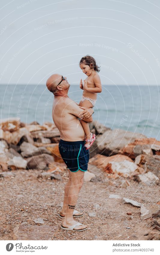 Grandfather and granddaughter having fun on rocky beach vacation grandfather ocean family elderly child girl water granddad nature shore enjoying retired