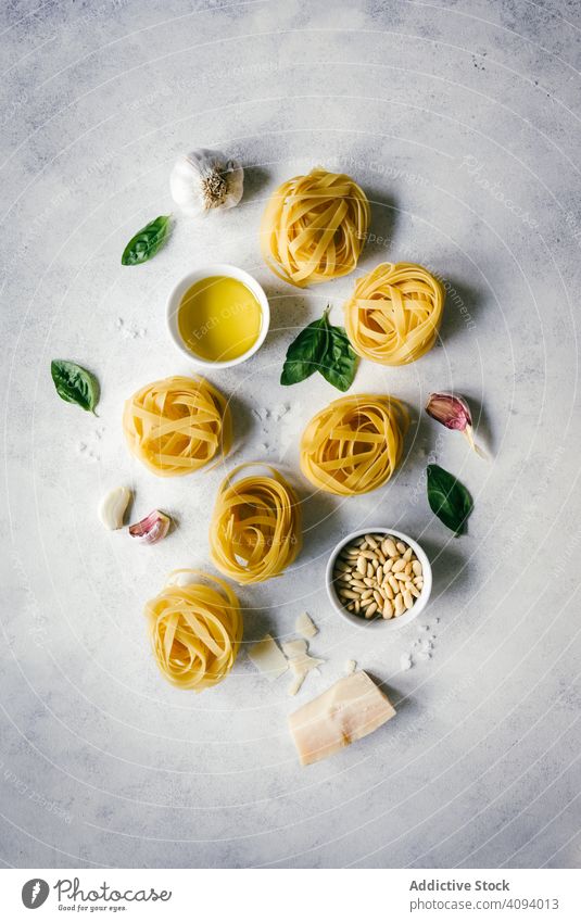 Nests of tagliatelle pasta with basil leaves and garlic on table nest pesto arranged raw pine nuts herbs white ingredient kitchen cheese cuisine tasty dry