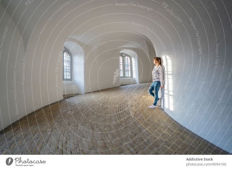 Casual woman leaning on wall in spacious gallery with windows observe travel architecture shadow interior calm peaceful relaxed minimalistic hall lobby arched
