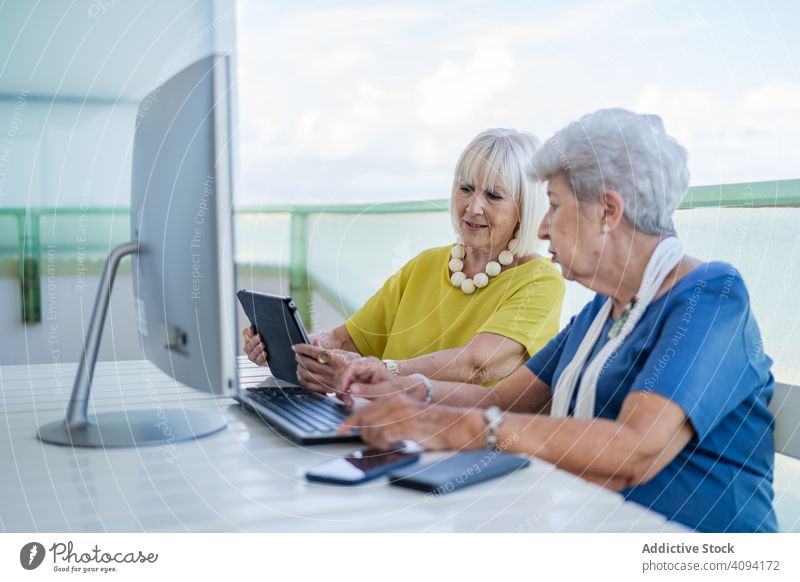 Elderly women using tablet near computer elderly friend balcony resort social media senior mature together friendship device gadget monitor terrace elegant