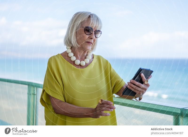 Elderly lady using smartphone on hotel terrace woman balcony sea resort elderly stylish retired female relax rest lifestyle pensioner mature senior trendy
