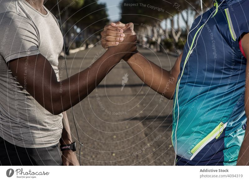 Pleased ethnic sportsmen in headphones shaking hands in park sportsman shake hands greeting meeting cheerful athletic training people sportswear friend stamina