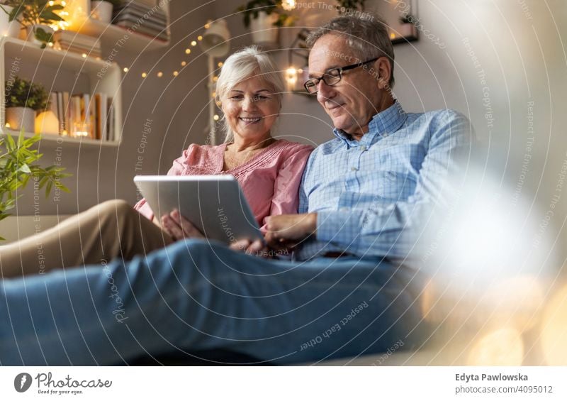 Mature couple using a tablet while relaxing at home people woman adult senior mature casual attractive female smiling happy Caucasian toothy enjoying two people