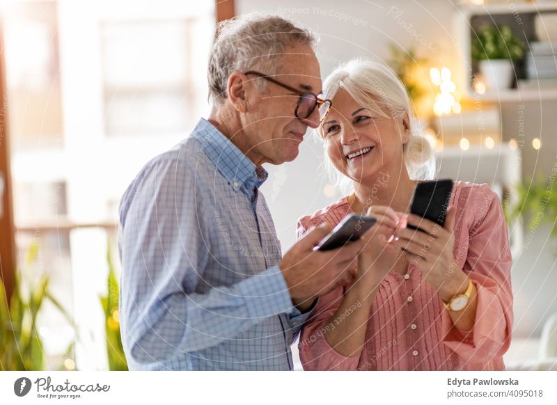 Senior couple using mobile phones at home people woman adult senior mature casual attractive female smiling happy Caucasian toothy enjoying two people love