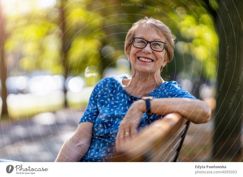 Portrait of a happy senior woman sitting on a bench people mature casual female Caucasian elderly old grandmother pensioner grandparent retired retirement