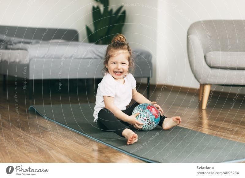 A small child plays on a sports mat with a ball healthy baby girl caucasian fun childhood happy cute kid smiling fitness toddler exercise beautiful little