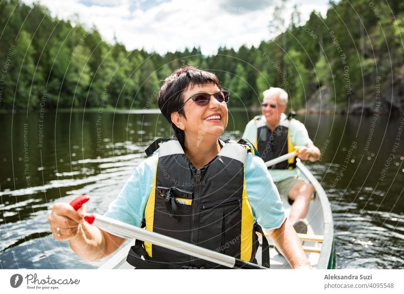 Happy mature couple in life vests canoeing in forest lake. Sunny summer day. Tourists traveling in Finland, having adventure. active activity beautiful discover