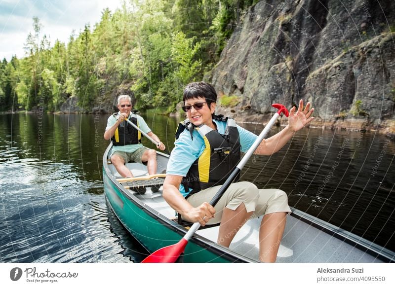 Happy mature couple in life vests canoeing in forest lake. Sunny summer day. Tourists traveling in Finland, having adventure. active activity beautiful discover