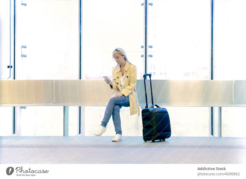 Lady traveler with suitcase using phone at airport woman sitting smartphone arrival tourism concentrated wait device vacation gadget call connection luggage